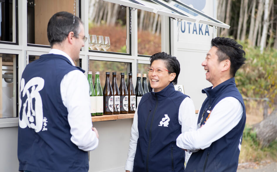 酒トラックの前で笑い合う男性3人組